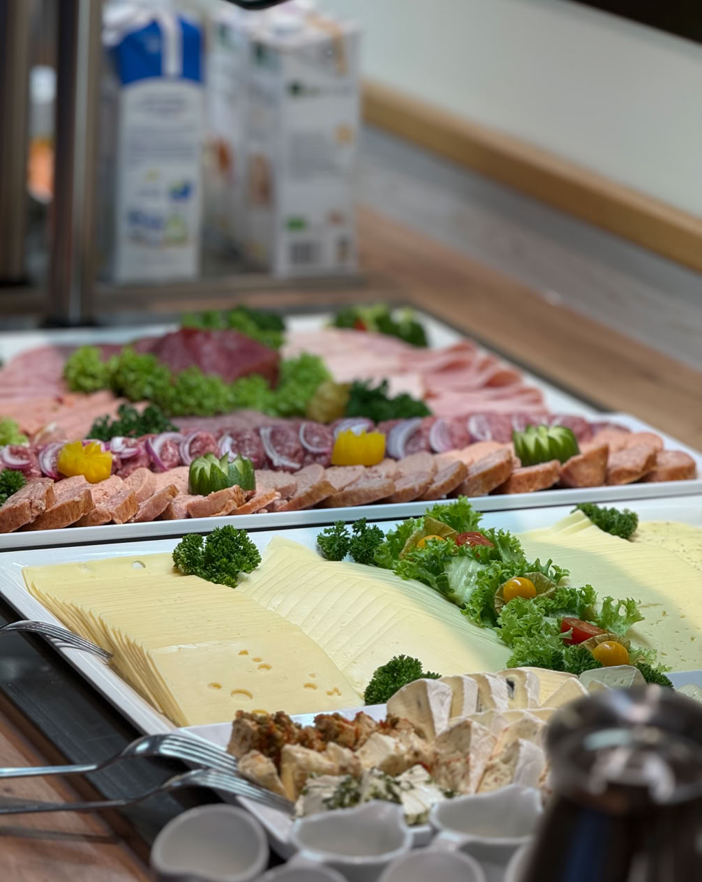Ein Tisch mit verschiedenen Lebensmitteln, darunter ein Korb mit Brötchen, eine Schale mit Butterstücken und mehrere Schalen mit Gewürzen oder Samen.